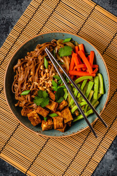 Soba noodles with vegetables and fried tofu in a bowl.