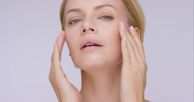 Face, luxury and mature woman with skincare, makeup and foundation against a grey studio background. Portrait, female person and model with wellness, luxury and beauty with pamper treatment and smile