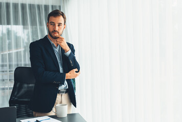 Handsome businessman in black suit stand confidently in his modern office portrait, deep in thought...