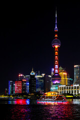 Tour boat cruises along the Huangpu River passing the iconic Oriental Pearl Tower and other colourful buildings lighting up the Shanghai night cityscape