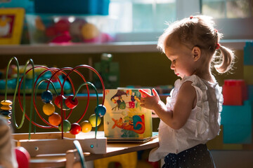 A cute little girl of 3 years old is playing educational toys in a kindergarten group. Portrait of...