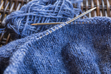 Blue wool yarn knitting on the metal needles with yarn ball, stockinette stitch knitted texture in progress close-up photo