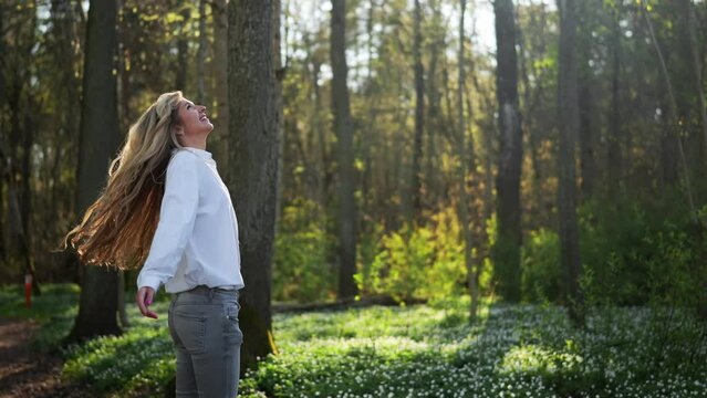 Young woman spinning with open arms in blooming spring forest