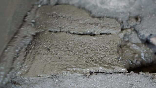A worker's gloved hand with a trowel fixes a hole in a concrete floor. Close-up.