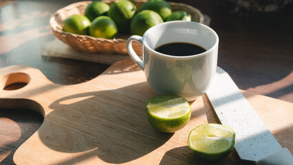 White mug with black coffee,hot espresso,americano on a wooden chopping board with a lemon slice and a white knife on wood table with sunlight warm morning, concept of healthy drink and detox colon.