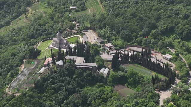 Aerial view of monastic complex of Bodbe nunnery on hillside among tall Cypress trees with Church of St. Nino on sunny day, Sighnaghi, Georgia