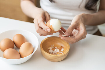 Protein in food, keto diet asian young woman hand peeling, shelling chicken boiled egg, prepares ingredient for breakfast meal on table at home. Removing egg shell, cleaning egg, health care concept. - obrazy, fototapety, plakaty