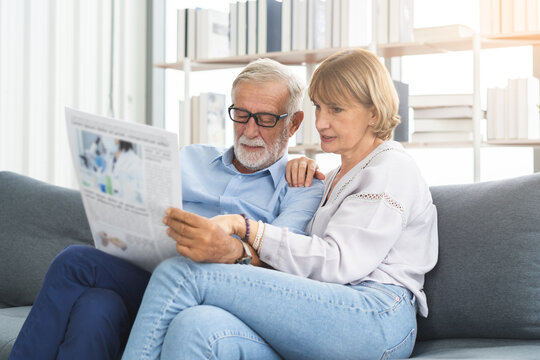 Happy husband and wife senior couple elderly family, caucasians mature, adult lover and retired man, woman reading newspaper,  report on sofa together at home. Husband and wife lifestyle.