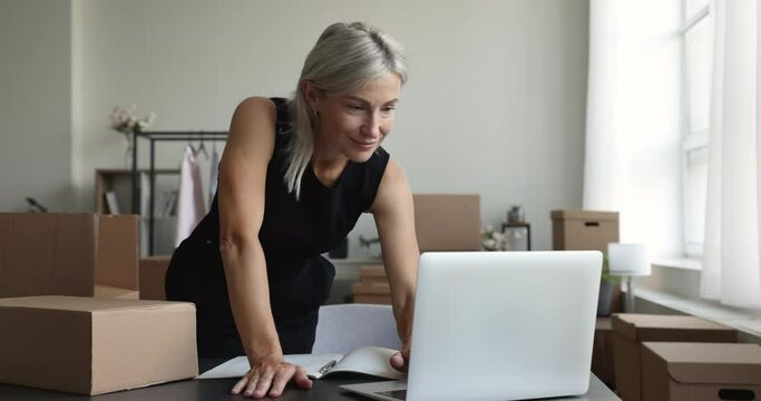 Positive mature internet store owner using laptop in home office, storage place, getting cheerful, happy, excited, making winner hand yes gesture, celebrating achievement, success, victory