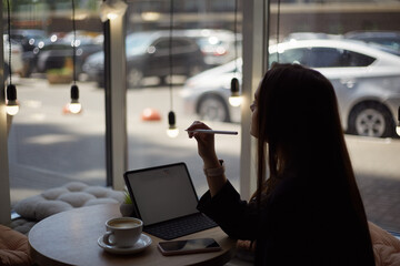 Graphic designer working in a cafe. Young creative female person creating a sketch with a stylus pen on a tablet computer. Freelance illustrator works in a restaurant
