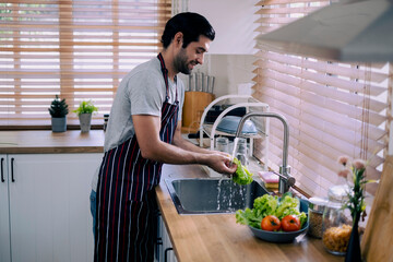 Arub man washing vegetable at sink in kitchen, gay preparing to make a meal at home on weekend with...