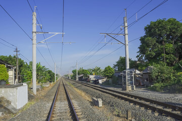 Perspective photo of Classic Railroad Train tracks with gravels, small stones, pebble rocks, and asphalt road. Bright Sunny Daylight during the day with blue sky background.