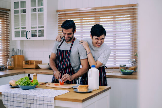 A couple of love preparing meal together with fun happiness and laugh in kitchen at home, boy touching his boyfriend shoulder with love - Powered by Adobe