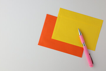 Gelber und orangefarbener Umschlag mit rosa Stift auf weißem Hintergrund