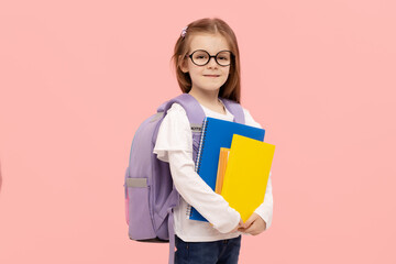 Portrait of a schoolgirl with textbooks and a backpack on a pink background. Back to school