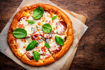 Pizza with spicy salami sausage, mozzarella cheese, tomato sauce and green basil on rustic wooden kitchen table background, top view