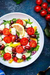 Tasty Greek salad with feta cheese, kalamata olives, tomatoes, paprika, cucumber and onion, healthy mediterranean food. Blue table background, top view