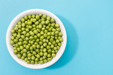 Fresh green peas in bowl isolated on blue background. Top view. Copy space