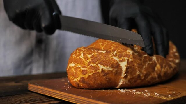 Cutting crispy bread with a knife in the kitchen. slow motion