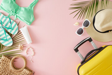 Sandy summer getaway concept. Top view flat lay of sunscreen bottle, yellow suitcase, beach accessories, palm leaves, seashells on pastel pink background with blank space for branding or promotion