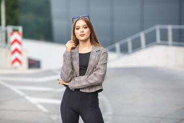 beautiful young girl with sunglasses in jacket posing near a modern office building with mirrored walls in a parking lot with road signs