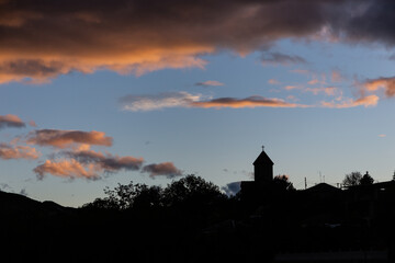 Silhouette of catholic church belfry sticking out above tree tops with sunset orange clouds in the sky in Akhaltsikhe town, Georgia.