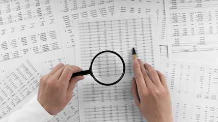 Woman holding a magnifying glass pointing at numbers on financial documents. ?oncept of finance, search and accounting.