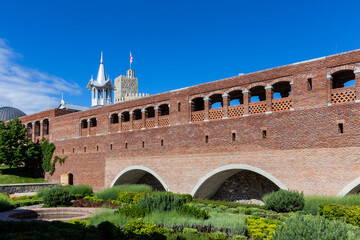 Fototapeta premium Red stone and brick bridge leading to Akhaltsikhe (Rabati) Castle, with cloisters and old moat overgrown with plants, flowers and grass, castle watchtower in the background.