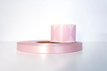 Pink coil of satin ribbon for labels or branding and roll of labels for thermal printing on printers. Clothing production.