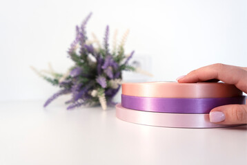 Woman's hand holding three coils of satin ribbons for labels or branding for clothing production.