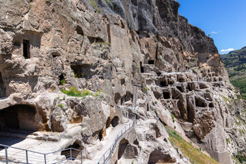 Vardzia cave monastery complex in Georgia, mountain slope with caves, tunnels and dwellings carved in the rock, Kura river valley in the background.