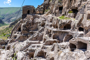 Vardzia cave monastery complex in Georgia, mountain slope with caves, tunnels and dwellings carved in the rock, bell tower building in the background. - obrazy, fototapety, plakaty
