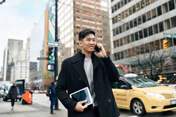 Young busy happy Asian business man office professional holding cellphone in hands walking on big...