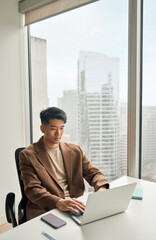 Busy professional Asian business man analyst working typing on laptop. Young Japanese serious businessman manager using computer technology thinking on financial market data in office, vertical shot.