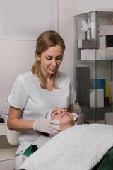 Top view of crop unrecognizable cosmetician using cotton pads and applying tonic on face of female customer lying on table in beauty salon during skincare procedure