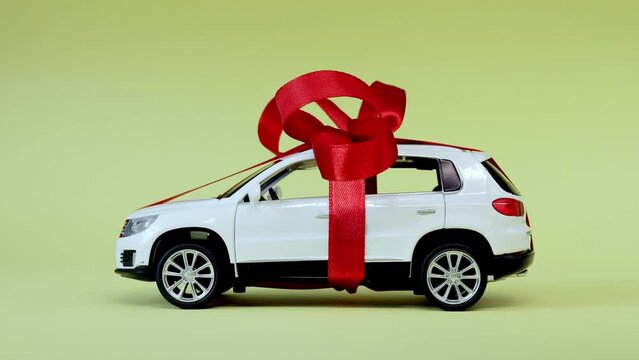 White model car with bow on a yellow background. Car as gift, surprise.