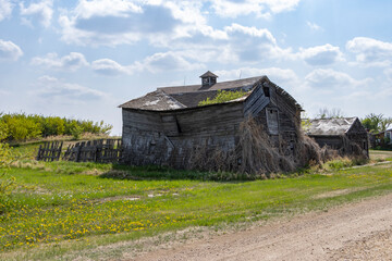 old abandoned barn in the countryside falling down, crumbling, with blue cloudy sky and green grass surrounding it