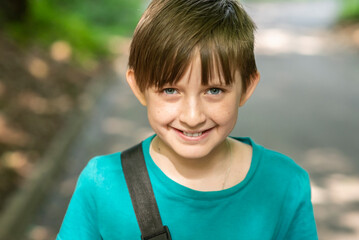smiling boy walking along the road through the green park