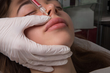 Close up of hands of cosmetologist making botox injection in female lips. She is holding syringe. The young beautiful woman is receiving procedure with enjoyment