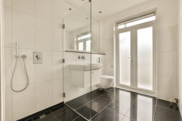 a modern bathroom with black and white tile flooring, glass shower door, and toilet in the corner area