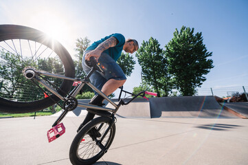 A middle-aged tattooed freestyle bmx rider is performing tricks and stunts in a skate park.
