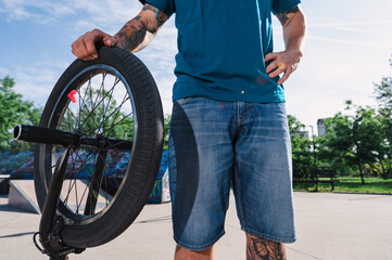 Cropped picture of a tattooed urban man leaning on his bmx in a skate park.