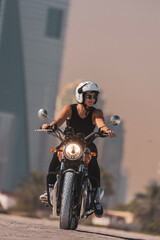 Fototapeta na wymiar woman driving a classic motorbike happy on a dubai beach with downtown in the background at sunset