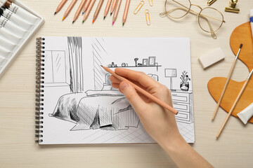 Woman sketching bedroom interior in notebook with pencil at wooden table, top view
