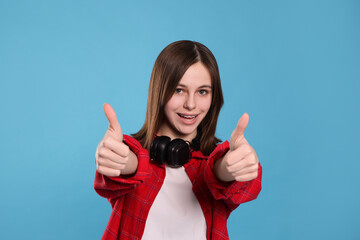 Portrait of smiling teenage girl showing thumbs up on light blue background