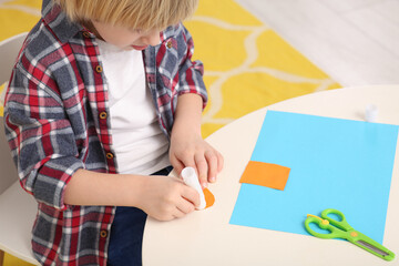 Boy using glue stick at desk in room, closeup. Home workplace