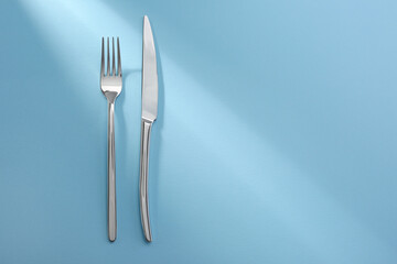 Shiny fork and knife on light blue background, flat lay. Space for text