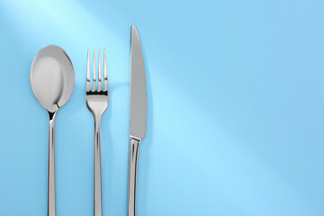 Spoon, fork and knife on light blue, flat lay. Space for text