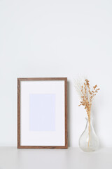 Empty photo frame and vase with dry decorative flowers on white table. Mockup for design