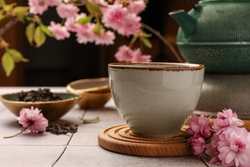 Traditional ceremony. Cup of brewed tea, teapot and sakura flowers on tiled table, closeup